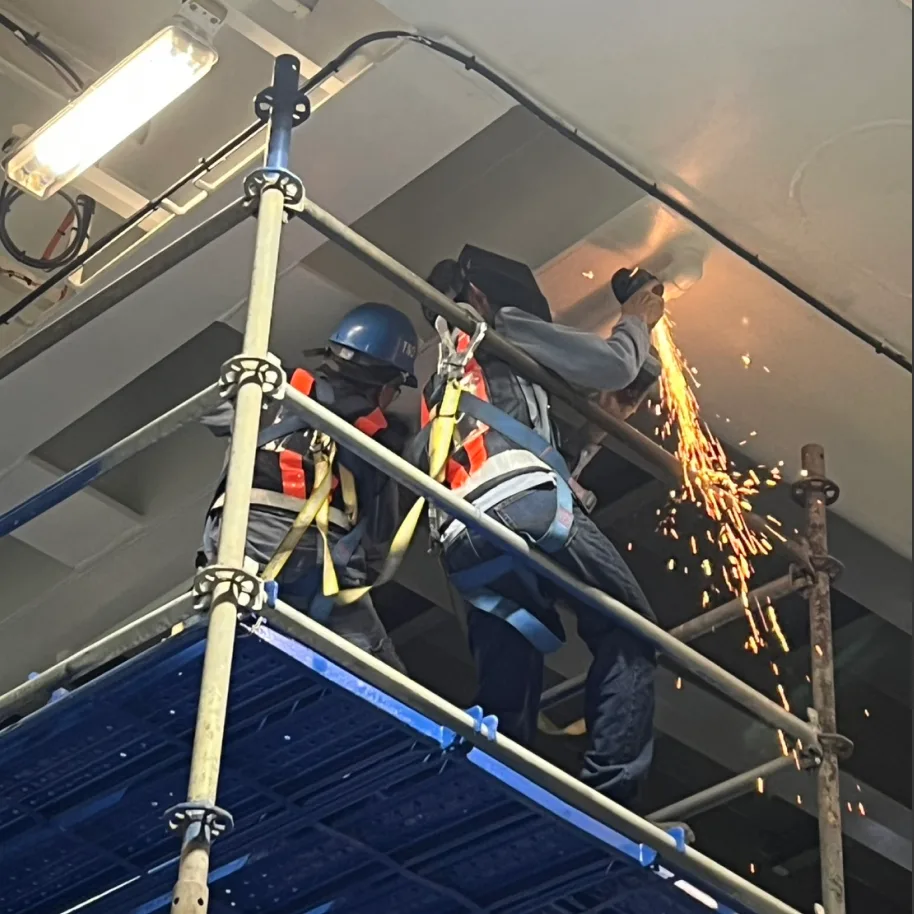 Cutting pipework at the deckhead, the sparks falling away past the edge of the staging.