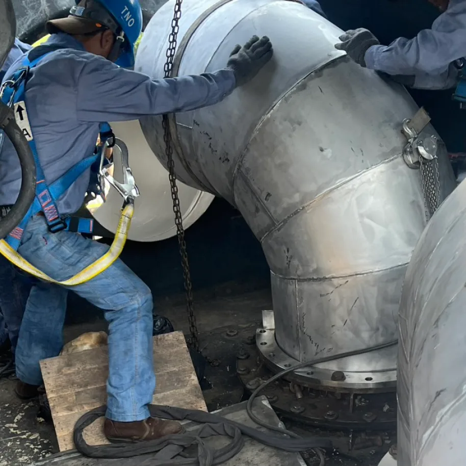 The bend landed over its bolted flange seat, the lift still taking the weight until the tacks are in.