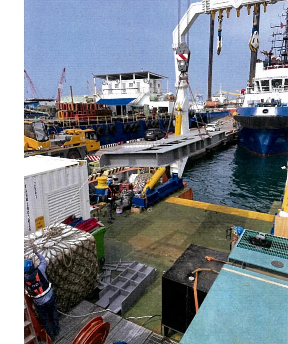 The deck before the work, with the ship's crane swinging a steel girder into position; the quay and other vessels lie beyond.