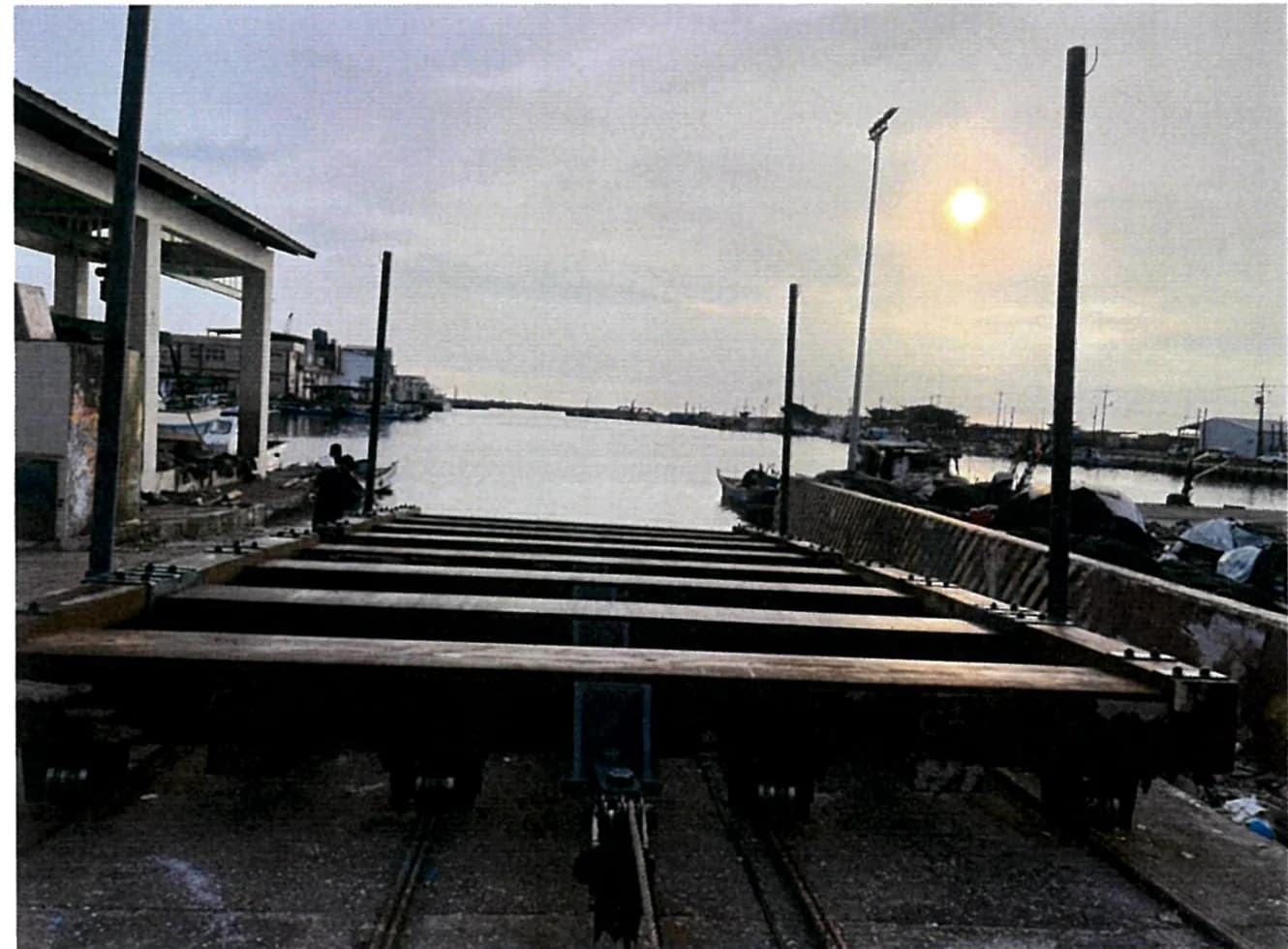The completed cradle standing on its rails, the launching slope ahead of it and the harbour's berths to either side.